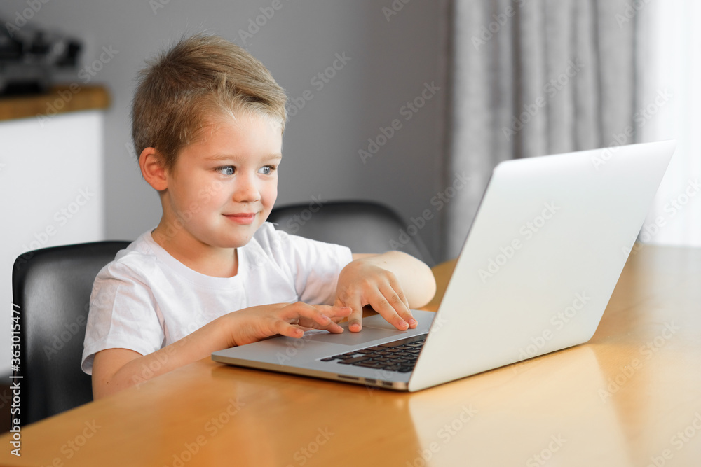 A young boy using a laptop computer sitting on top of a tableundefined at home A young boy using a laptop computer sitting on top of a tableundefined at home