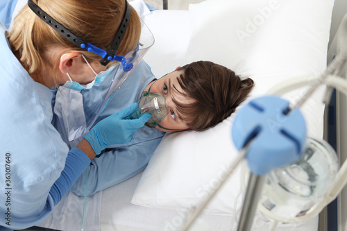 nurse takes care of the patient child in hospital bed playing with teddy bear, wearing protective masks, corona virus covid 19 protection concept,