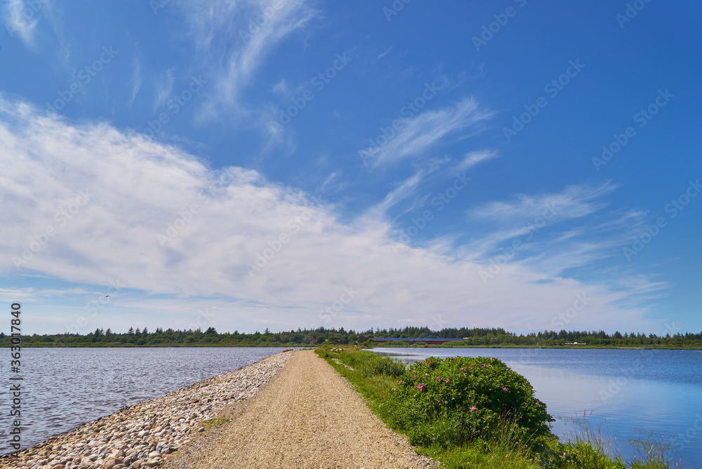 Straight gravel footpath at the dam in the lake Filsø (Denmark) under vivid blue sky an white clouds