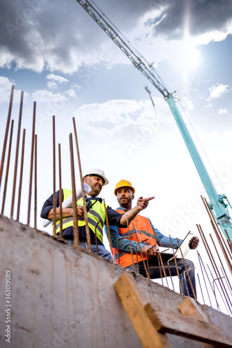 Fotografi Men in hardhat and yellow and orange jacket posing on building site