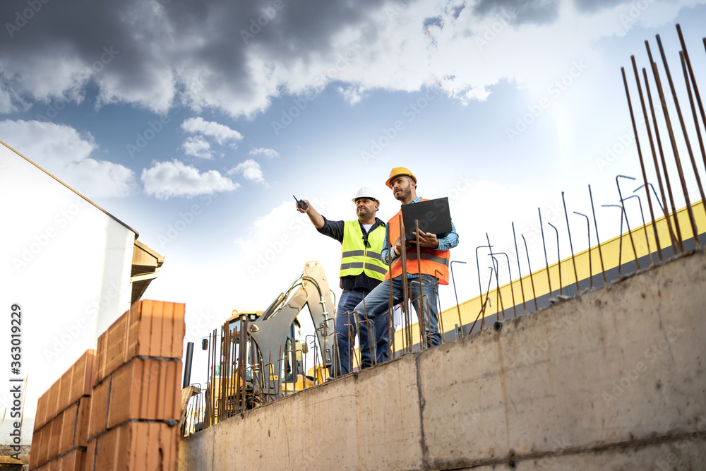 Men in hardhat and yellow and orange jacket posing on building site Men in hardhat and yellow and orange jacket posing on building site