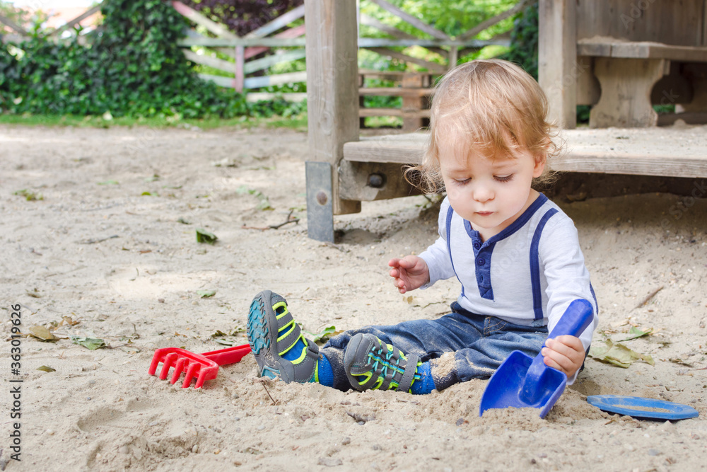 Cute little child having fun playing with sand and colorful toys in the park, beautiful summer sunny day in children playground Cute little child having fun playing with sand and colorful toys in the park, beautiful summer sunny day in children playground