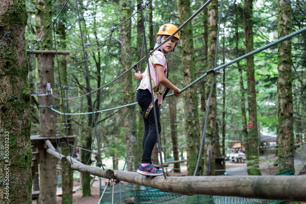Tree climbing activity installations wooded area.  A child walks on wooden bars.