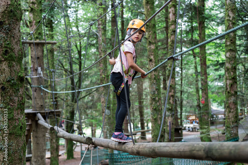 Tree climbing activity installations wooded area. A child walks on wooden bars.