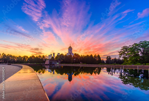 Dawn over Victory Park on Poklonnaya Hill in Moscow in the summer. Colorful blue sky with clouds and sunrise on the horizon above an Orthodox church. The sky is reflected in the pool of the fountain.
