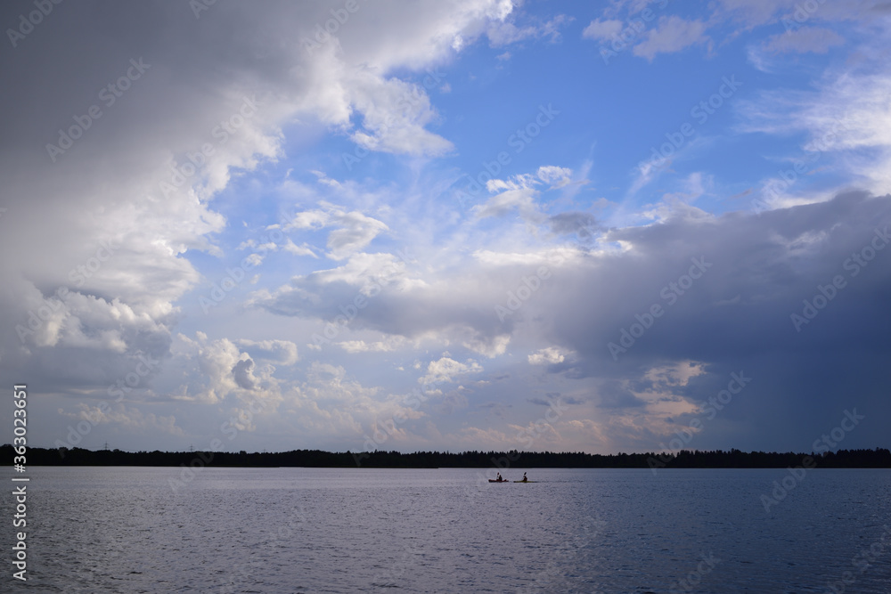 On a lake, a small rowboat drives in the distance under dark storm clouds