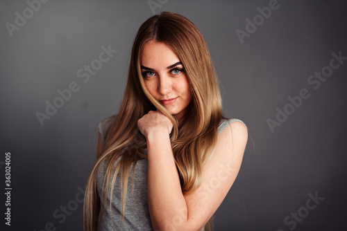 A girl with blue eyes looks piercingly into the frame, wrapping her hair in a gray background