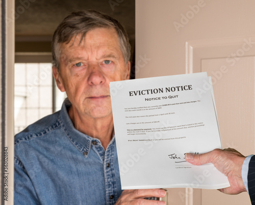 Open front door with man in suit handing an eviction notice to a defaulting renter in modern home due to missed rent