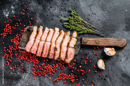 Grilled sliced pork steak on a meat cleaver. Organic meat. Black background. Top view