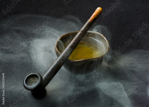 Smoking pipe and a bowl of hot tea on a dark background