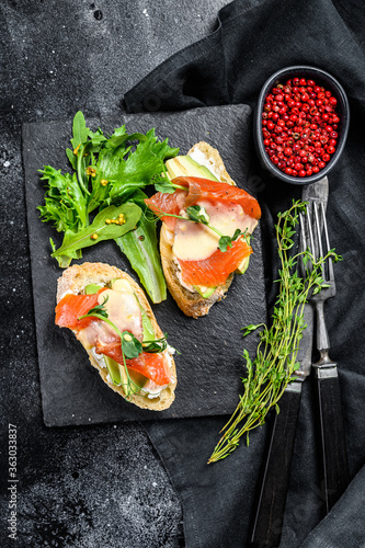 Healthy sandwich with avocado and salmon. Spinach and arugula salad. Black background. Top view