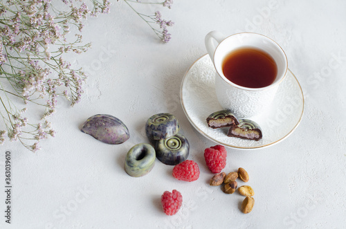  Raw vegan candy with raspberry and pistachio filling in chocolate coating. Served with a cup of tea on a light background,healthy sweets. Vintage. Copy space 