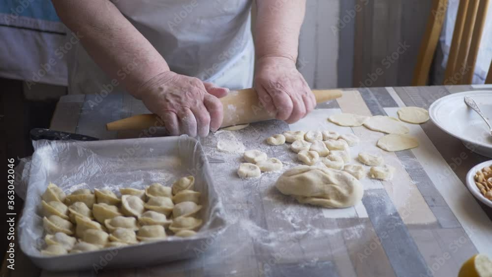 Beautiful elderly woman with wrinkled hands prepares dough on kitchen table. Knife, minced meat and condiments for pies. shallow depth of field Beautiful elderly woman with wrinkled hands prepares dough on kitchen table. Knife, minced meat and condiments for pies. shallow depth of field
