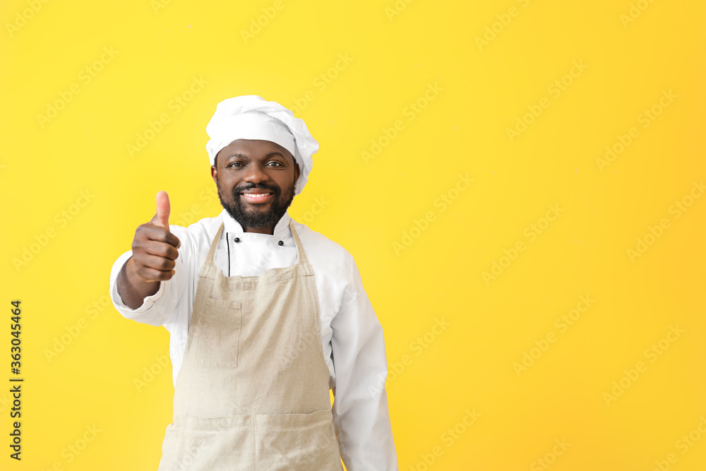 Male African-American chef showing thumb-up on color background