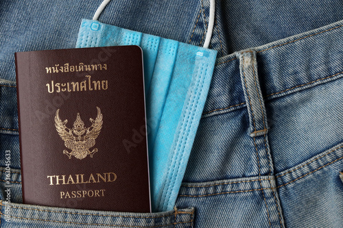 Tourism and traveling concept in New Normal after Covid-19 / Coronavirus pandemic. Thai Passport travel with blurred medical mask and in jeans pocket with copy space.