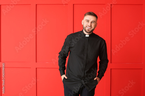 Handsome young priest on color background photo