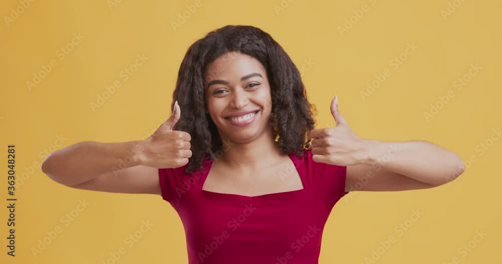 Positive black woman showing thumbs up and widely smiling Positive black woman showing thumbs up and widely smiling