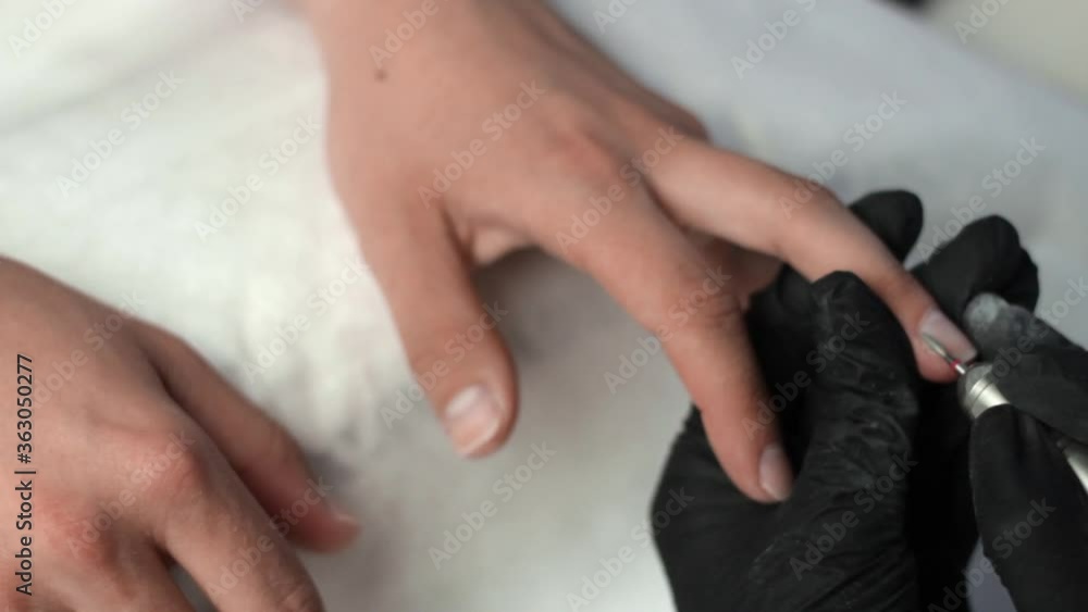 Manicurist using an electric nail drill to polish and remove cuticles on the fingernails of a client Manicurist using an electric nail drill to polish and remove cuticles on the fingernails of a client