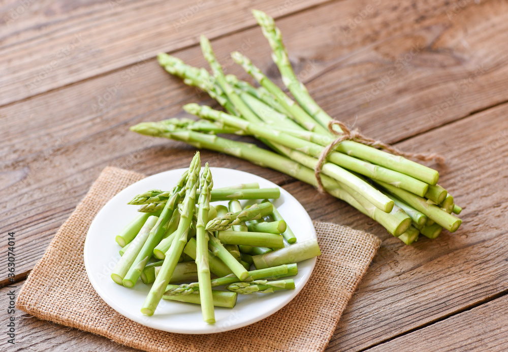 Asparagus on white plate and wooden background - Fresh green asparagus sliced for cooking food Asparagus on white plate and wooden background - Fresh green asparagus sliced for cooking food