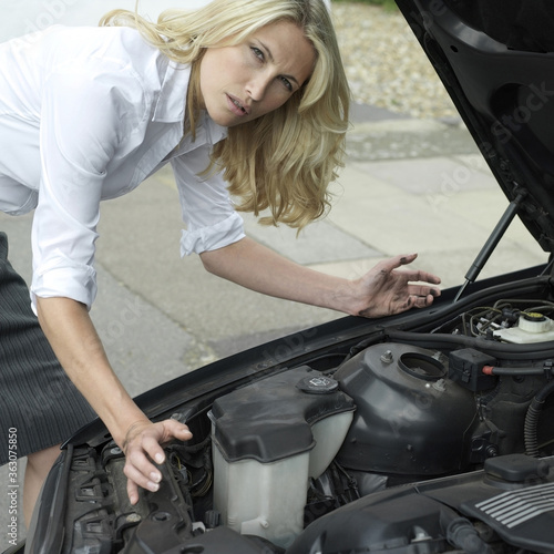 Businesswoman looking under car hood © ImageHit