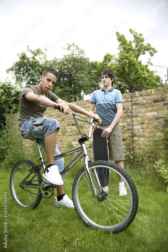 Boy riding on bicycle, another boy holding a skateboard Boy riding on bicycle, another boy holding a skateboard