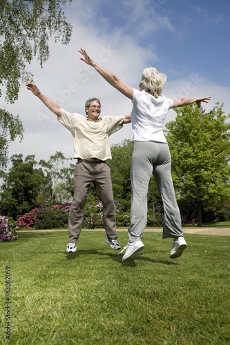 Senior man and woman jumping with their arms outstretched