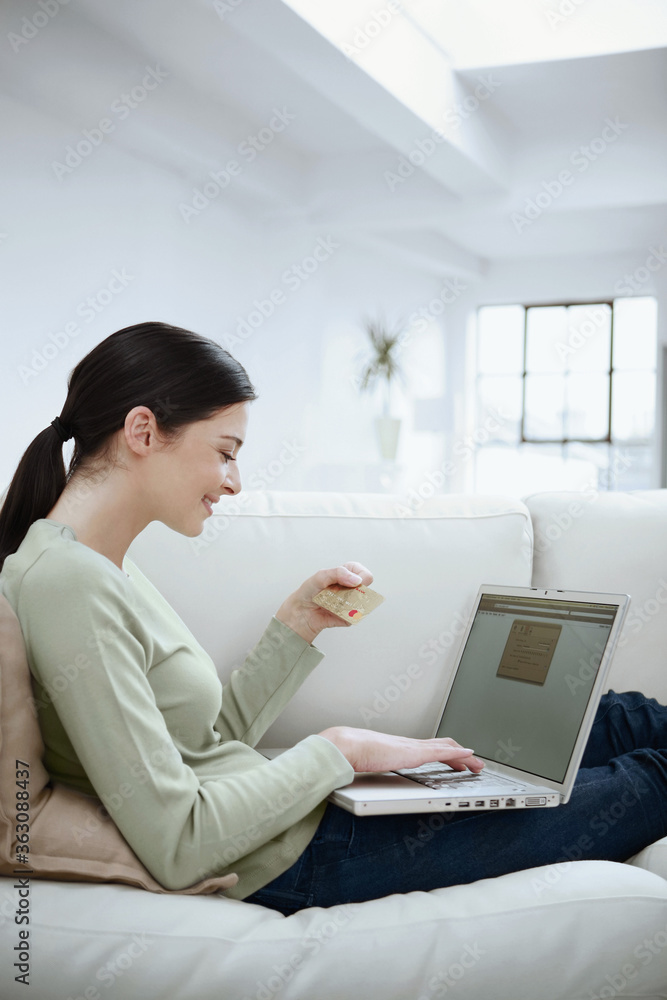 Woman looking at credit card while using laptop Woman looking at credit card while using laptop