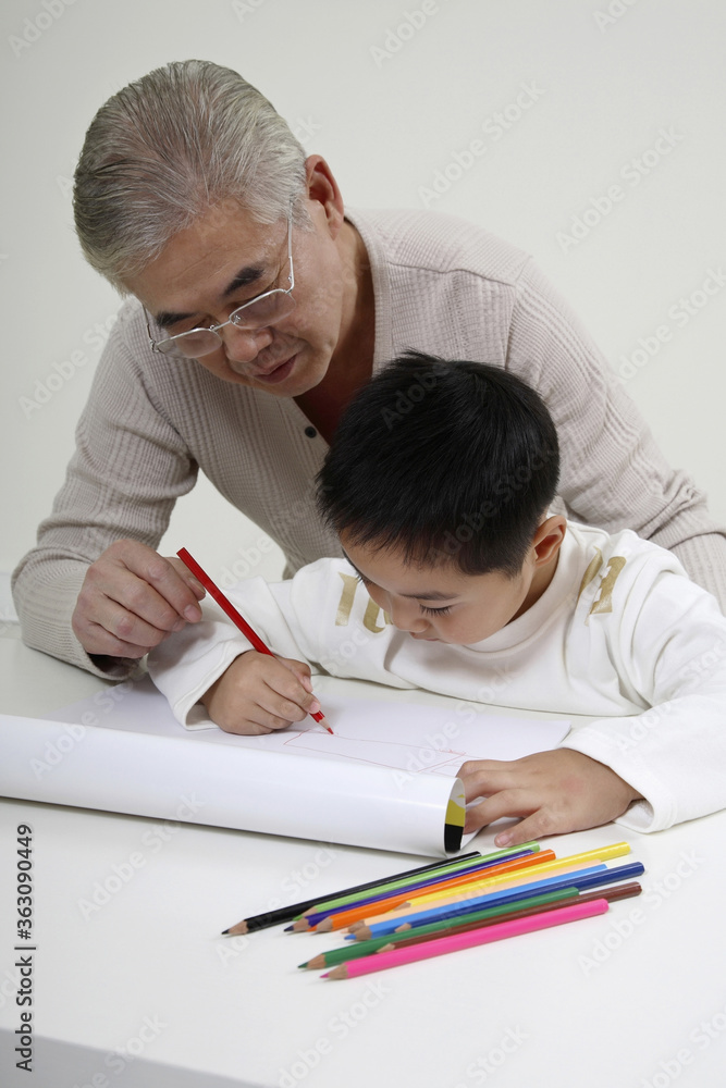 Boy drawing with coloured pencil, senior man watching Boy drawing with coloured pencil, senior man watching