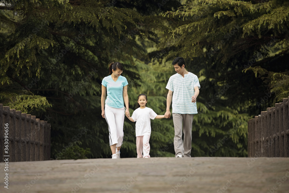 Girl holding hands with parents while walking in the park Girl holding hands with parents while walking in the park