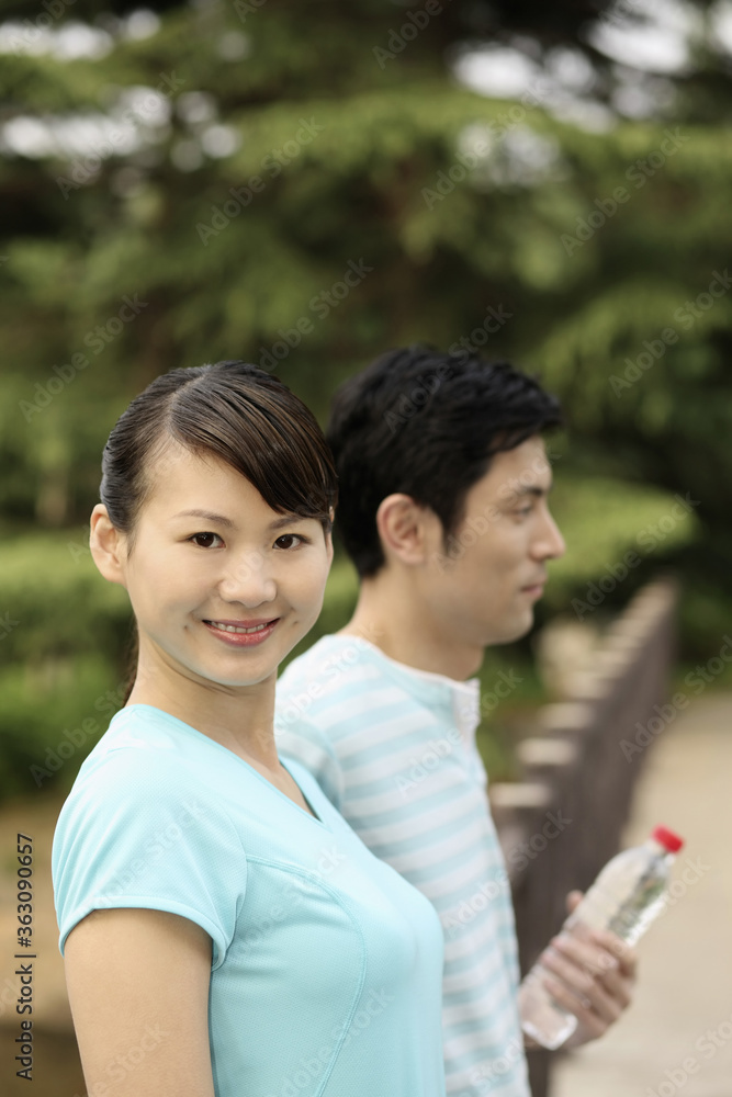 Woman smiling, man holding water bottle in the background Woman smiling, man holding water bottle in the background