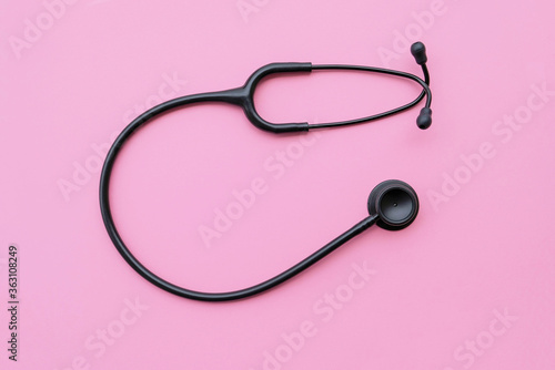 Black modern stethoscope on pastel pink background.