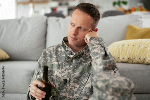 Depressed soldier with bottle sitting in livig room., Alcohol addiction.	 photo