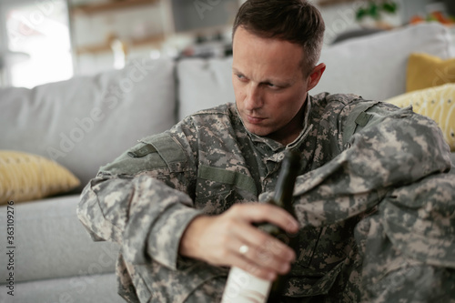 Depressed soldier with bottle sitting in livig room., Alcohol addiction. 