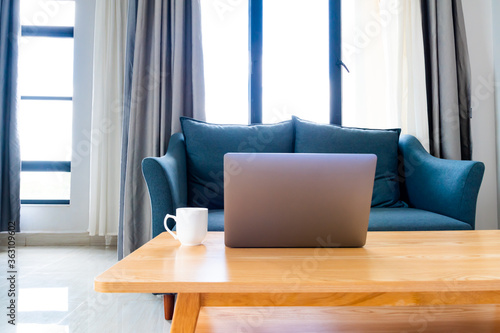 Laptop on wooden table with sofa in cozy room  set up for work from home workstation online learning.