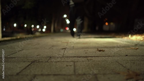 Man walking down a paved footpath on river embankment lit by lanterns at night in autumn. Salgir River Embankment in Simferopol. photo