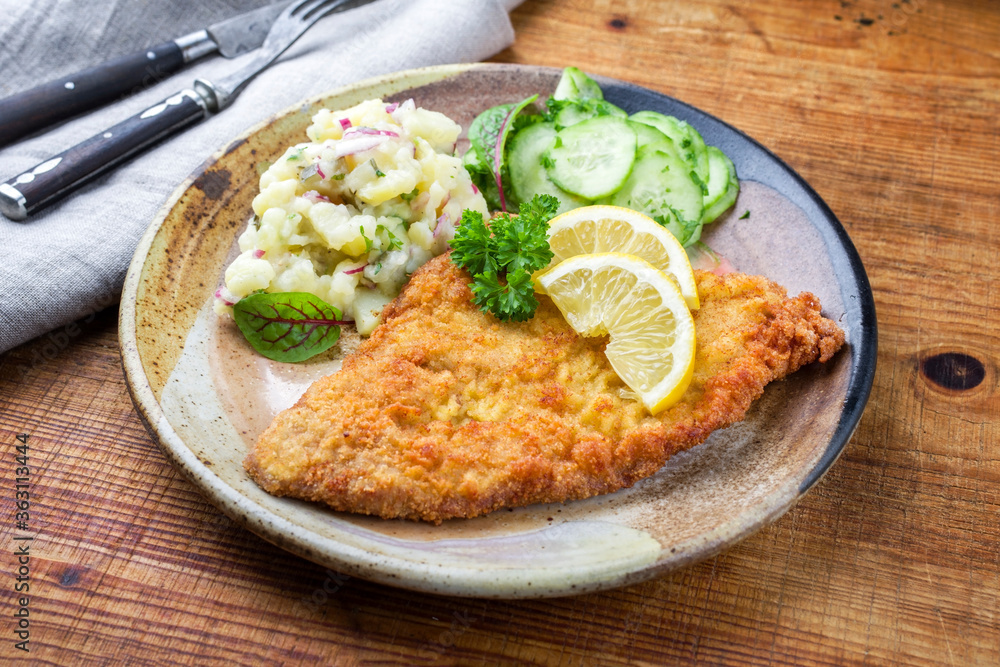 Traditioneles frittiertes Wiener Schnitzel vom Kalb mit Kartoffel und Gurkensalat angeboten als close-up auf einem rustikalen design Teller auf einem Holz Board Traditioneles frittiertes Wiener Schnitzel vom Kalb mit Kartoffel und Gurkensalat angeboten als close-up auf einem rustikalen design Teller auf einem Holz Board