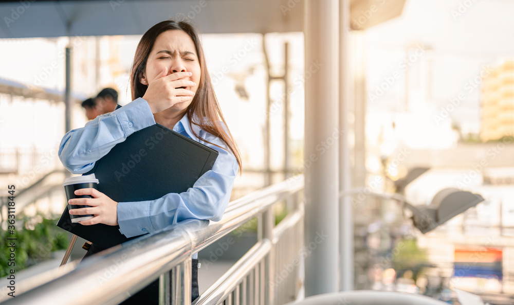 Woman office worker is going to work in the morning with a file and coffee with unhappy and sleepy.