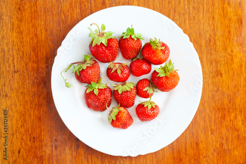 Ripe strawberries on a white plate on a wooden table  top view