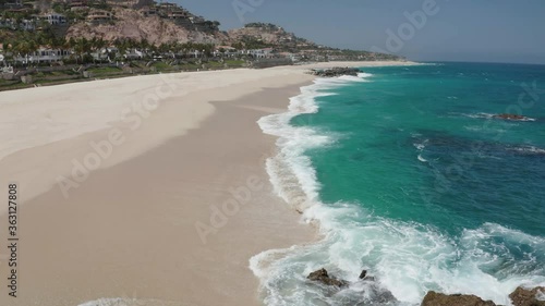 Drone tilts up to reveal beautiful Cabo San Lucas beach resort. Blue water, sunny day. 