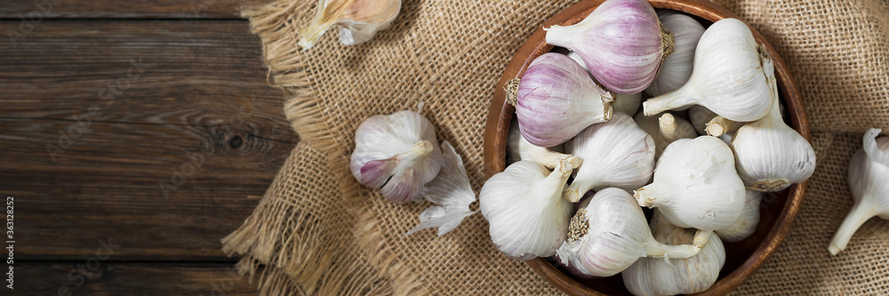 Garlic in a wooden bowl on a wooden table. lots of garlic in a bowl. Garlic close-up. Banner with space for text