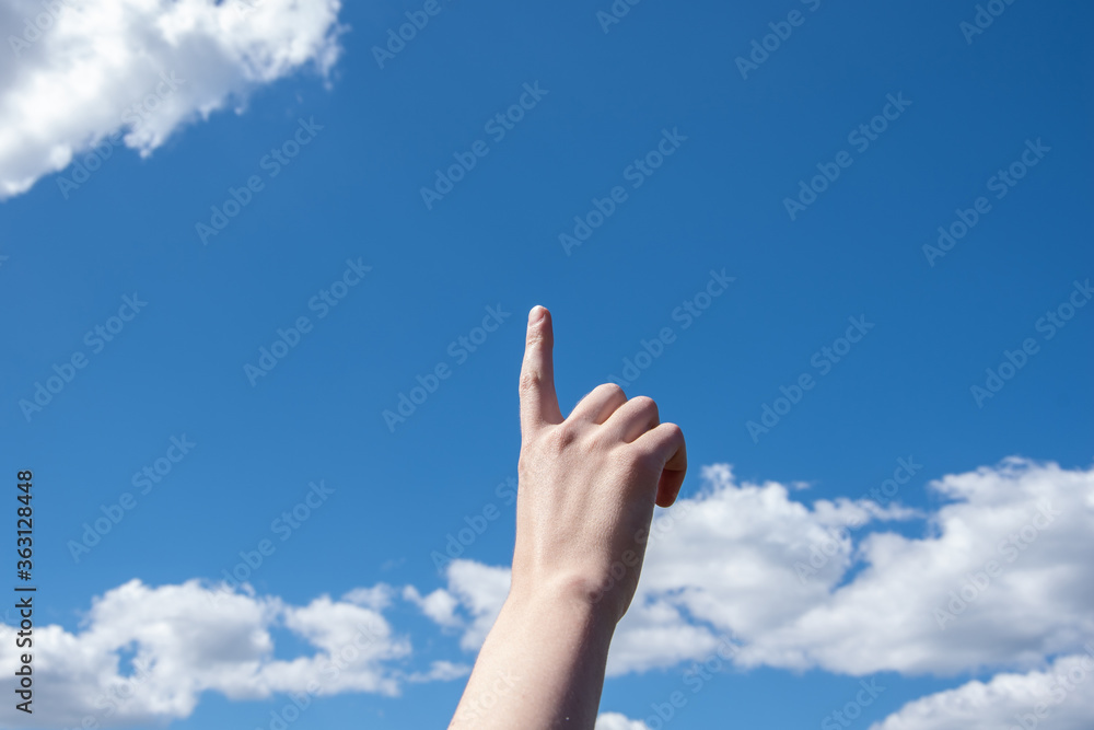 Close-up female hand with index finger up on a background of blue sky with clouds, copy space Close-up female hand with index finger up on a background of blue sky with clouds, copy space