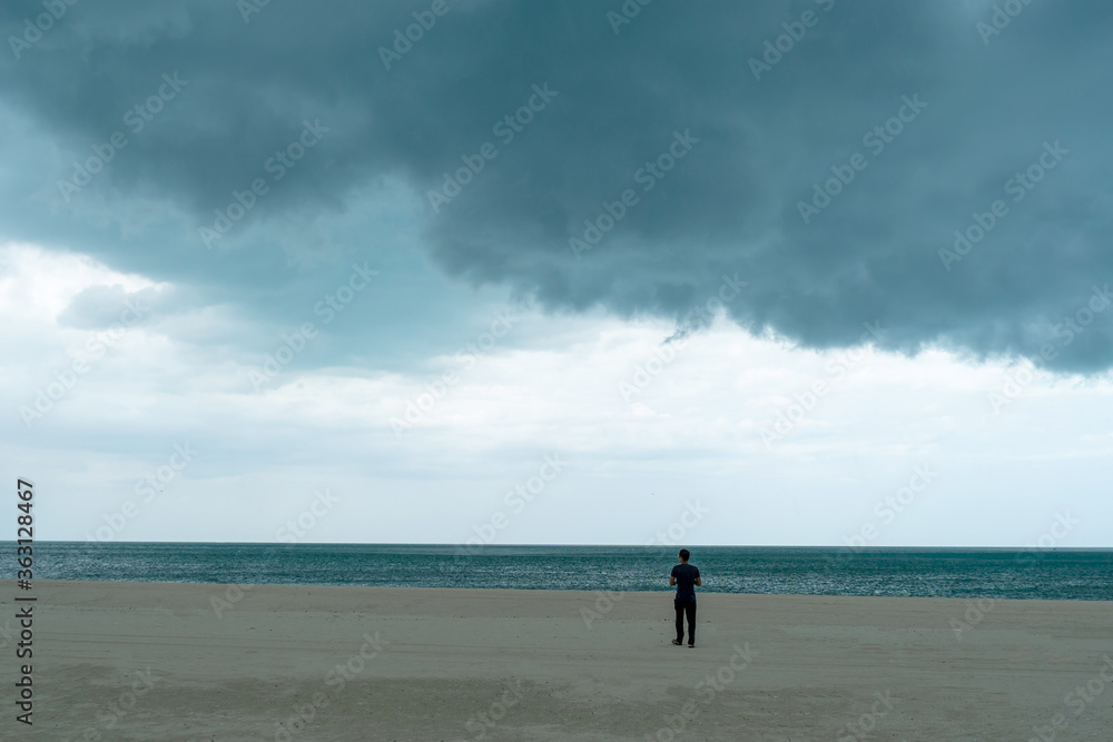 Man standing in beach with dark huge cloud sky black stormy cloud motion in big rain day.