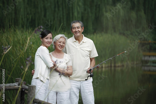 Senior man fishing on a dock, senior woman and woman posing beside him