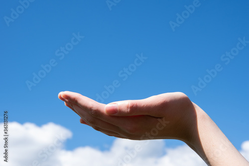 Empty open female hand on a background of blue sky with clouds. Can be used as a basis for design, copy space.