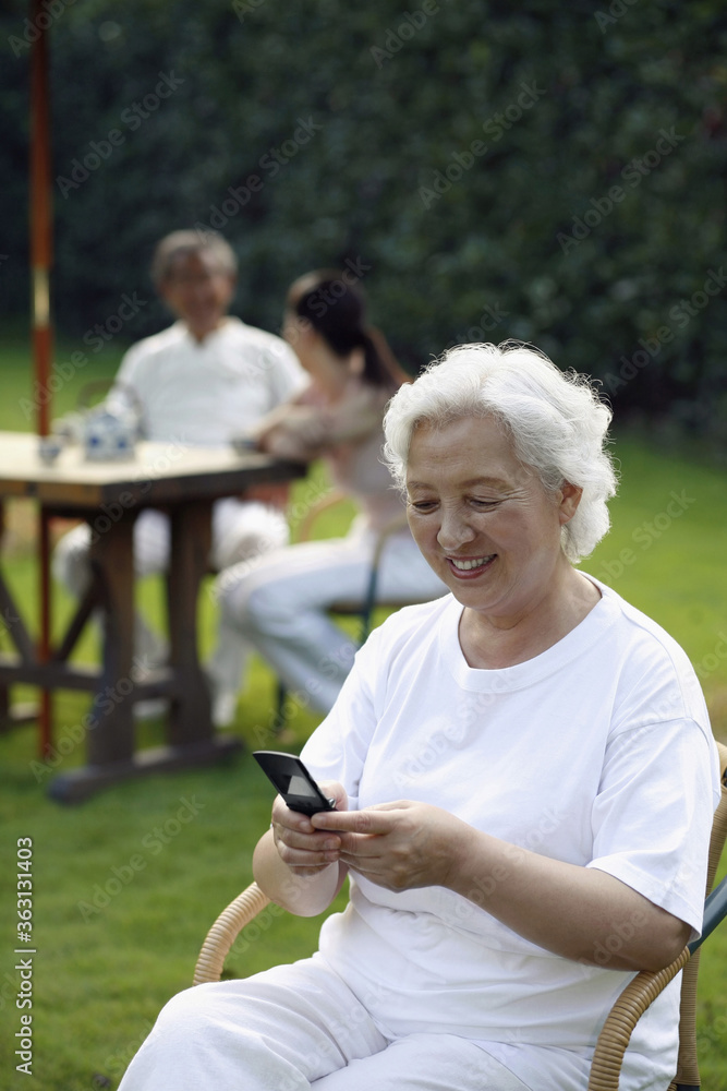 Senior woman text messaging on the phone, woman having tea with senior man in the background Senior woman text messaging on the phone, woman having tea with senior man in the background