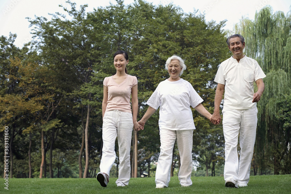 Woman together with senior couple holding hands while walking in the park Woman together with senior couple holding hands while walking in the park