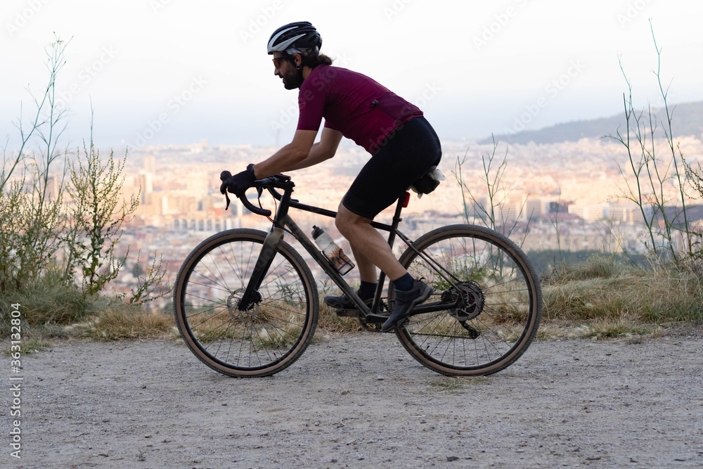 Male cyclist with gravel bike at full speed with the city of Barcelona on the horizon Male cyclist with gravel bike at full speed with the city of Barcelona on the horizon