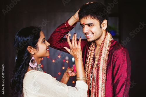 Indian woman is giving blessings to the man by putting tika on his forehead while wearing traditional ethnic clothes