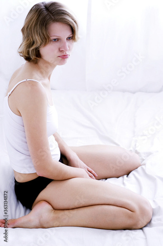 Side shot of a woman in white camisole sitting on the bed