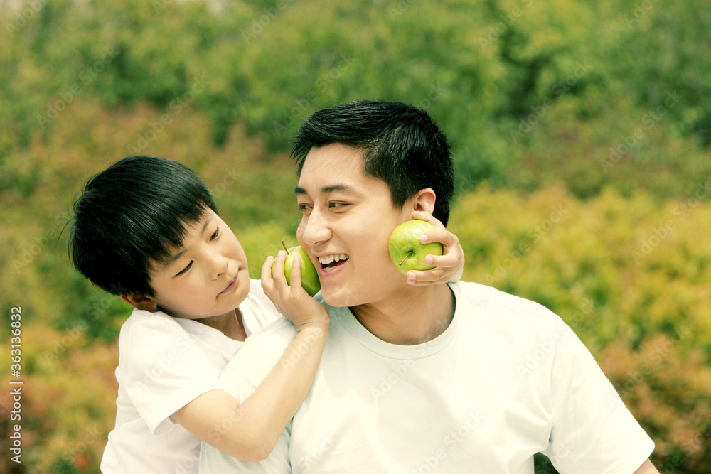 A boy playfully placing two green apples on his father's cheeks A boy playfully placing two green apples on his father's cheeks